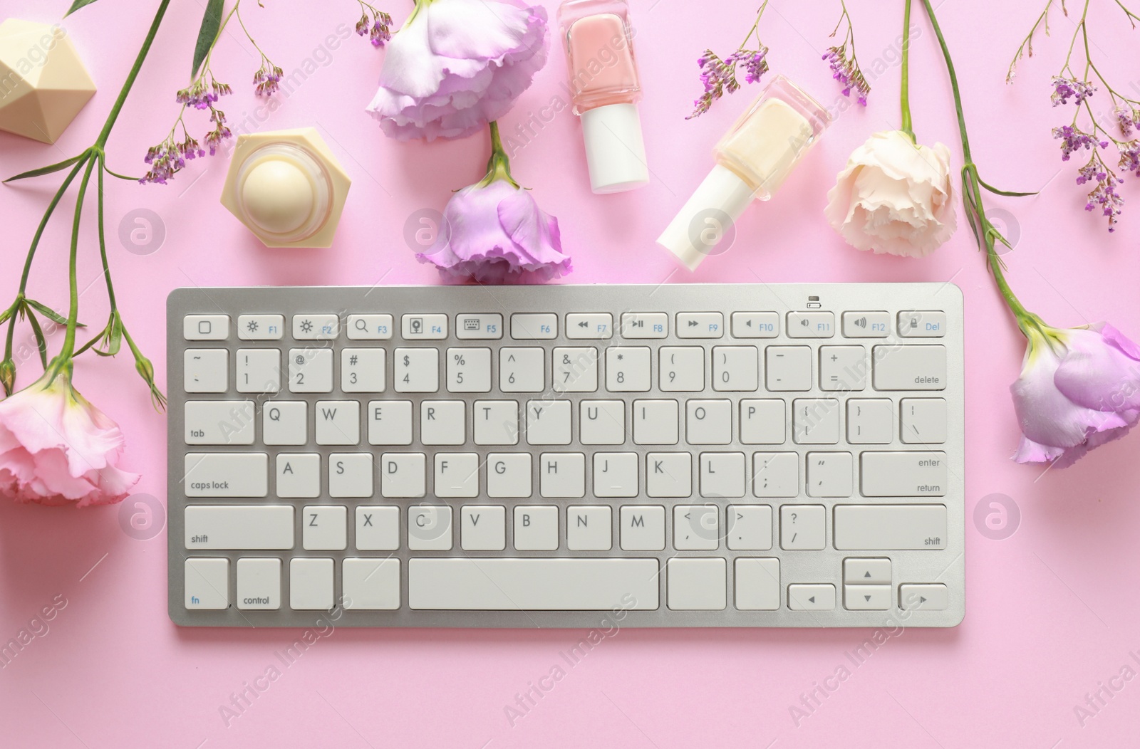 Photo of Flat lay composition with keyboard and flowers on pink background. Beauty blogger's workplace