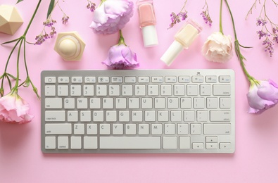 Flat lay composition with keyboard and flowers on pink background. Beauty blogger's workplace