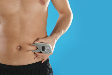 Photo of Man measuring body fat layer with digital caliper on light blue background, space for text. Nutritionist's tool
