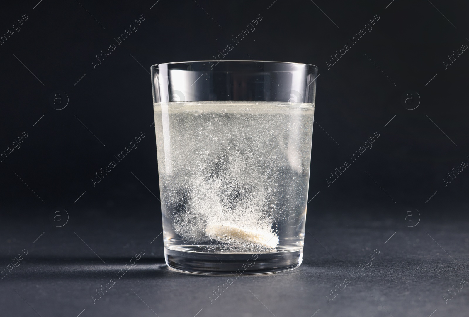 Photo of Effervescent pill dissolving in glass of water on grey table