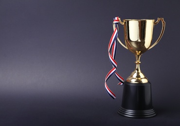 Golden trophy cup with ribbon on grey background. Space for text