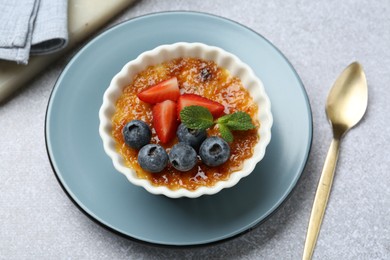 Photo of Delicious creme brulee with berries and mint in bowl served on grey textured table, above view