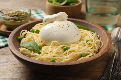 Photo of Bowl of delicious pasta with burrata, peas and spinach on wooden table
