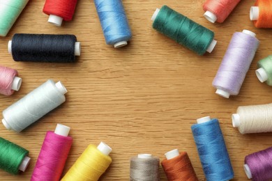 Photo of Many colorful sewing threads on wooden table, flat lay. Space for text