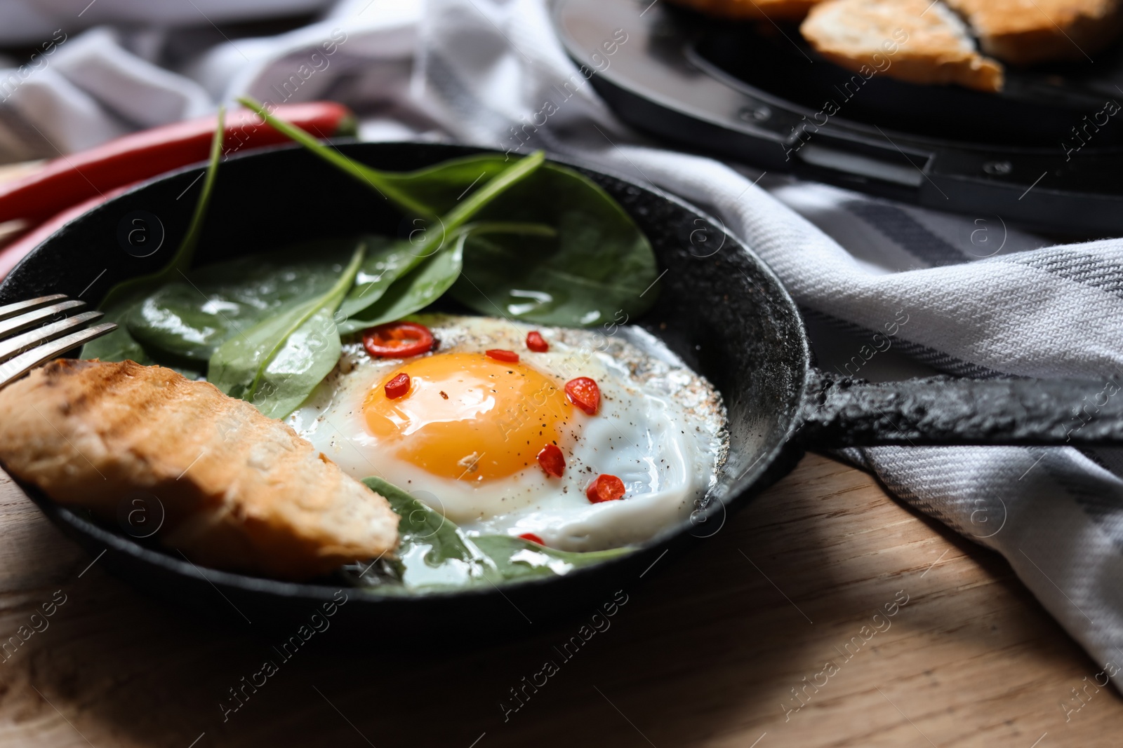 Photo of Delicious fried egg with spinach and chilli served on wooden table, closeup