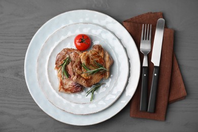 Photo of Delicious fried meat with rosemary and tomato served on grey wooden table, flat lay