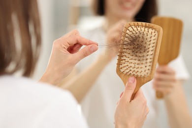 Photo of Woman taking her lost hair from brush near mirror indoors, closeup. Alopecia problem