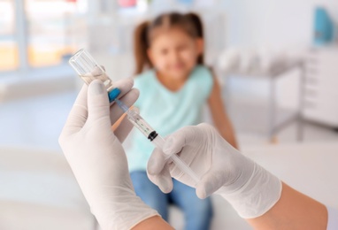 Photo of Doctor filling syringe with medicine and child on background. Vaccination day