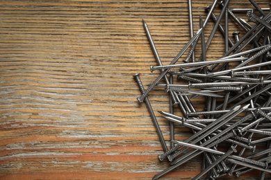 Photo of Many metal nails on wooden background, flat lay. Space for text