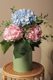 Photo of Beautiful hortensia flowers in can on wicker stand indoors
