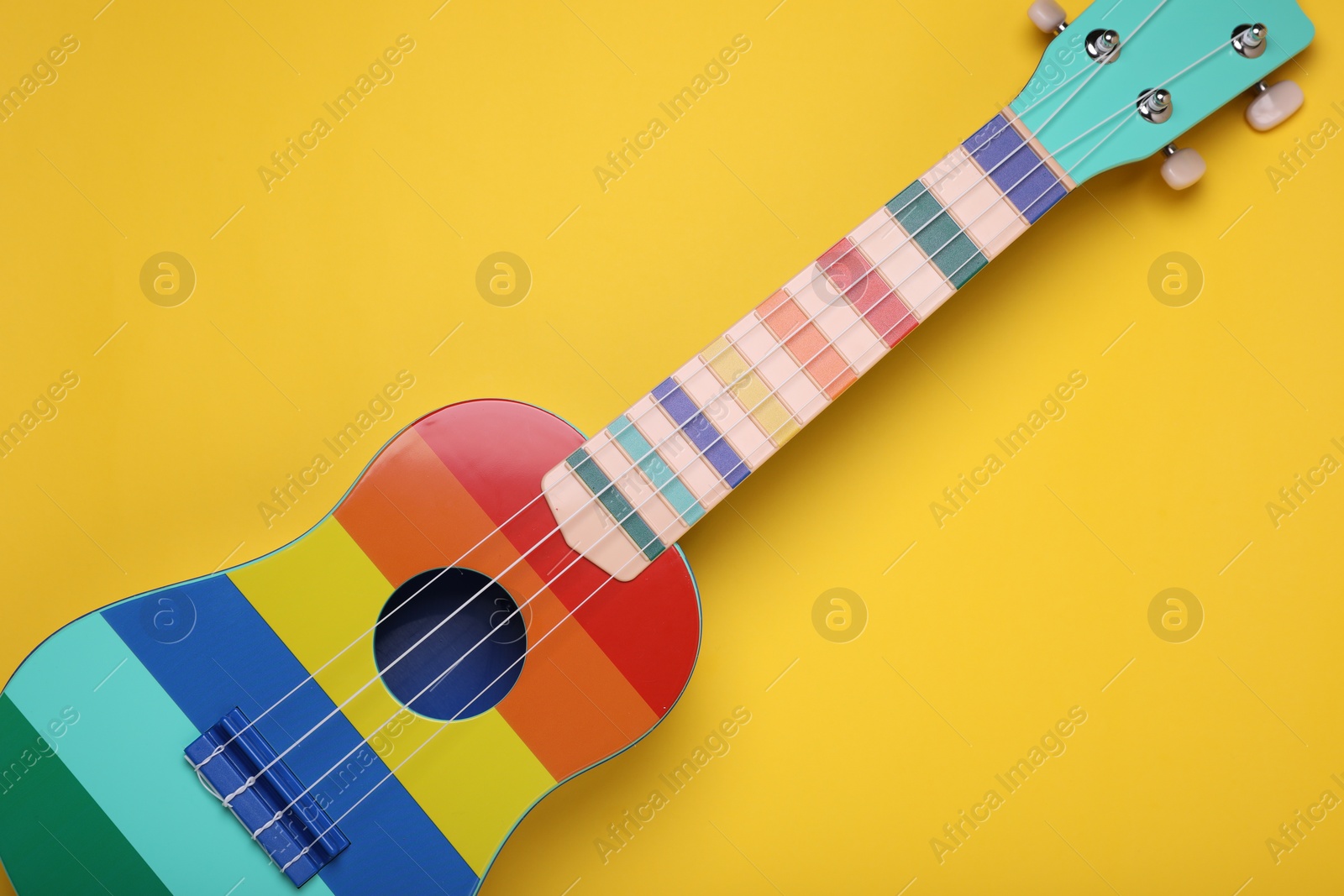 Photo of Colorful ukulele on yellow background, top view. String musical instrument