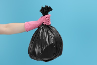 Photo of Woman holding plastic bag full of garbage on light blue background, closeup