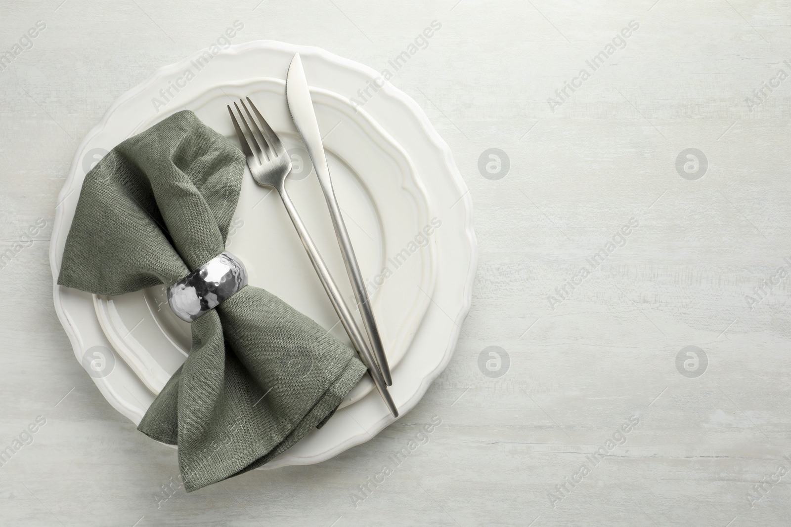 Photo of Stylish setting with cutlery, napkin and plates on light textured table, top view. Space for text