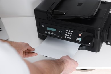 Photo of Man using modern printer at white desk in office, closeup