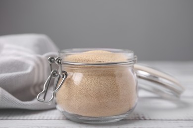 Photo of Granulated yeast in glass jar on white wooden table, closeup