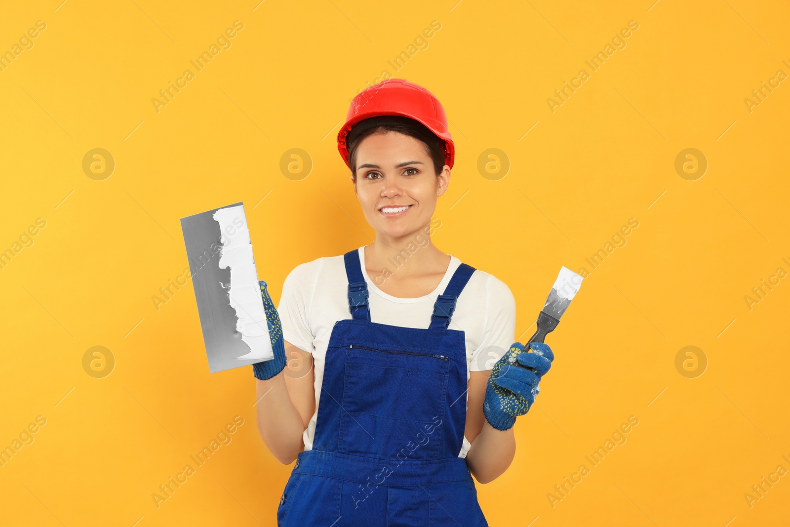 Photo of Professional worker with putty knives in hard hat on orange background