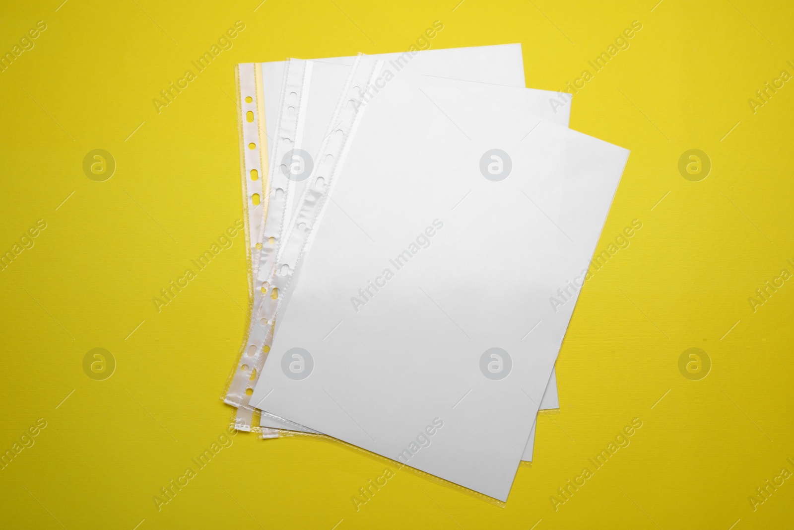 Photo of Punched pockets with paper sheets on yellow background, flat lay
