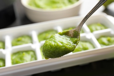 Photo of Puree in spoon near ice cube tray on table, closeup. Ready for freezing