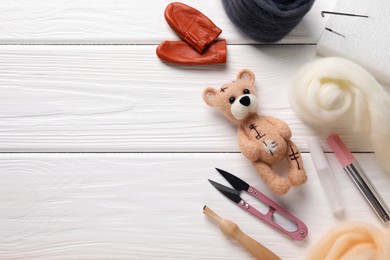 Photo of Felted bear, wool and tools on white wooden table, flat lay. Space for text