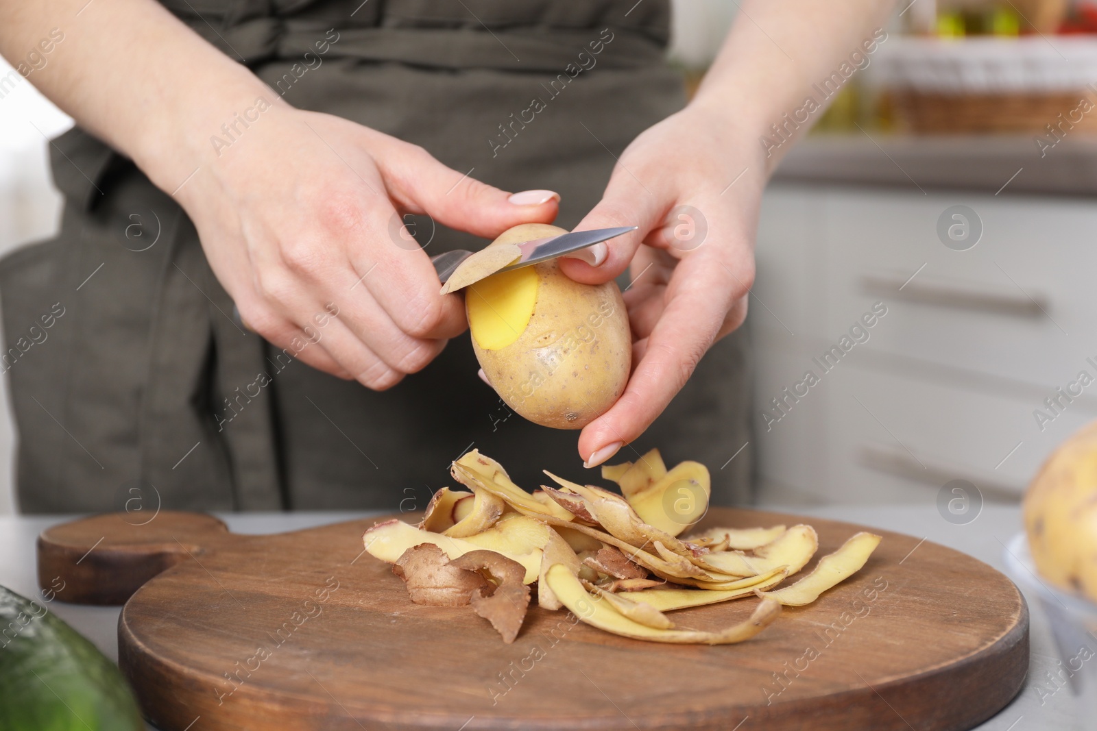 Photo of Woman peeling fresh potato with knife at table indoors, closeup