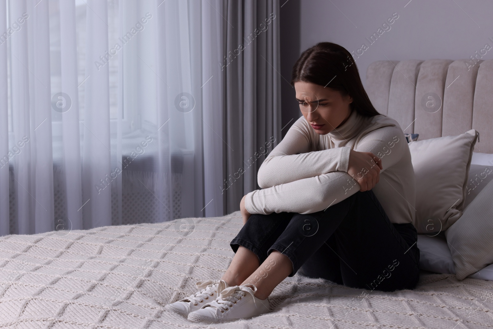 Photo of Sad young woman on bed at home, space for text. Loneliness concept