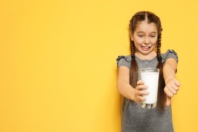 Little girl with dairy allergy holding glass of milk on color background