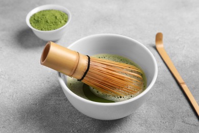 Photo of Cup of matcha tea and bamboo whisk on light gray textured table
