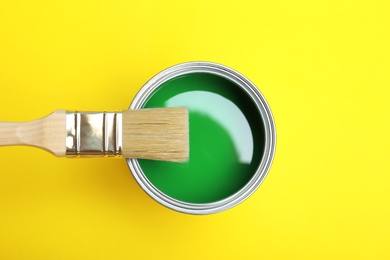 Photo of Paint can and brush on yellow background, top view