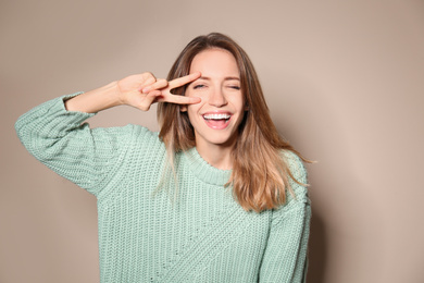 Happy young woman wearing warm sweater on beige background