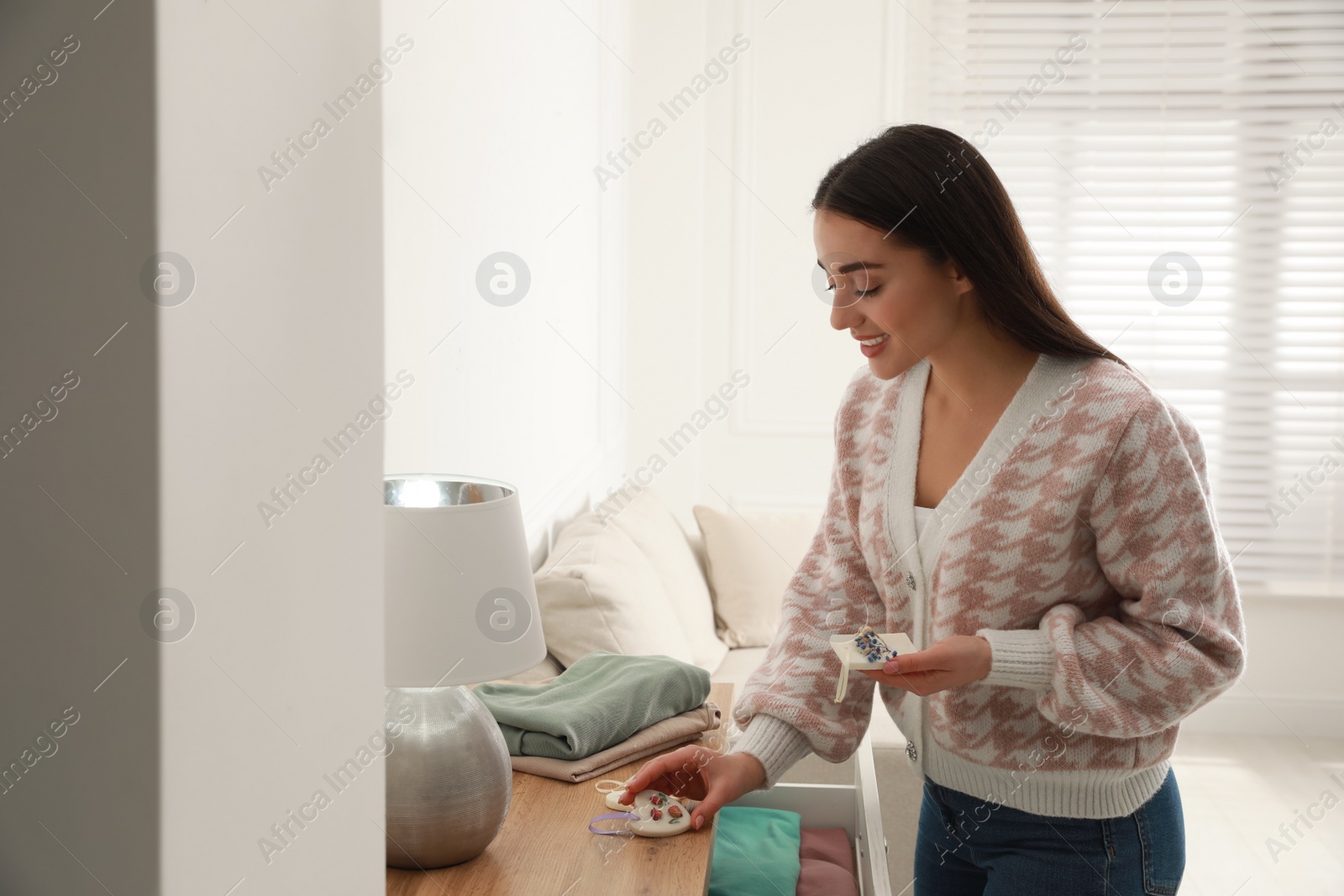 Photo of Young woman with scented sachets in room