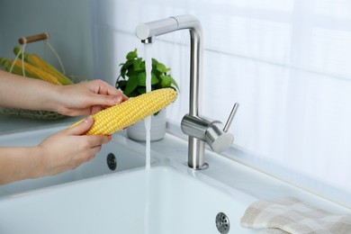 Photo of Woman washing corn cob in kitchen, closeup