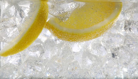 Photo of Juicy lemon slices and ice cubes in soda water against white background, closeup