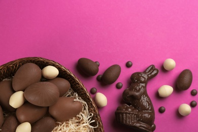 Photo of Flat lay composition with chocolate Easter bunny, candies and eggs on pink background. Space for text