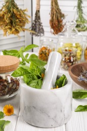 Photo of Mortar with pestle and many different medicinal herbs on white wooden table