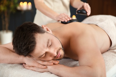 Handsome man receiving hot stone massage in spa salon