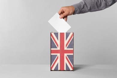 Image of Man putting his vote into ballot box decorated with flag of United Kingdom against light background, closeup