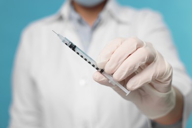 Doctor holding syringe on light blue background, closeup