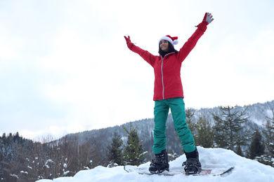 Photo of Young snowboarder wearing Santa hat on snowy hill. Winter vacation