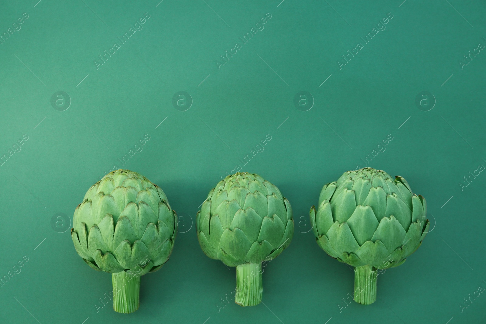 Photo of Whole fresh raw artichokes on green background, flat lay. Space for text