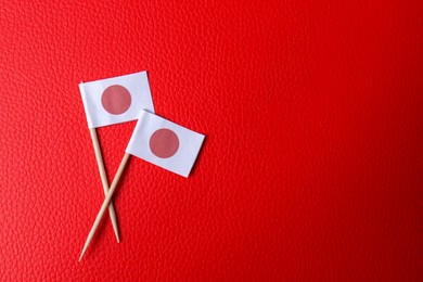 Photo of Small paper flags of Japan on red textured background, flat lay. Space for text