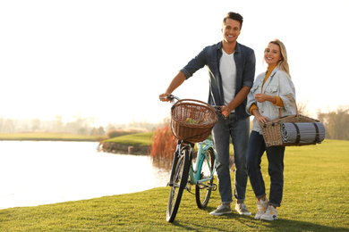 Photo of Young couple with bicycle and picnic basket near lake on sunny day