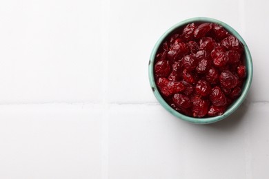 Tasty dried cranberries in bowl on white tiled table, top view. Space for text