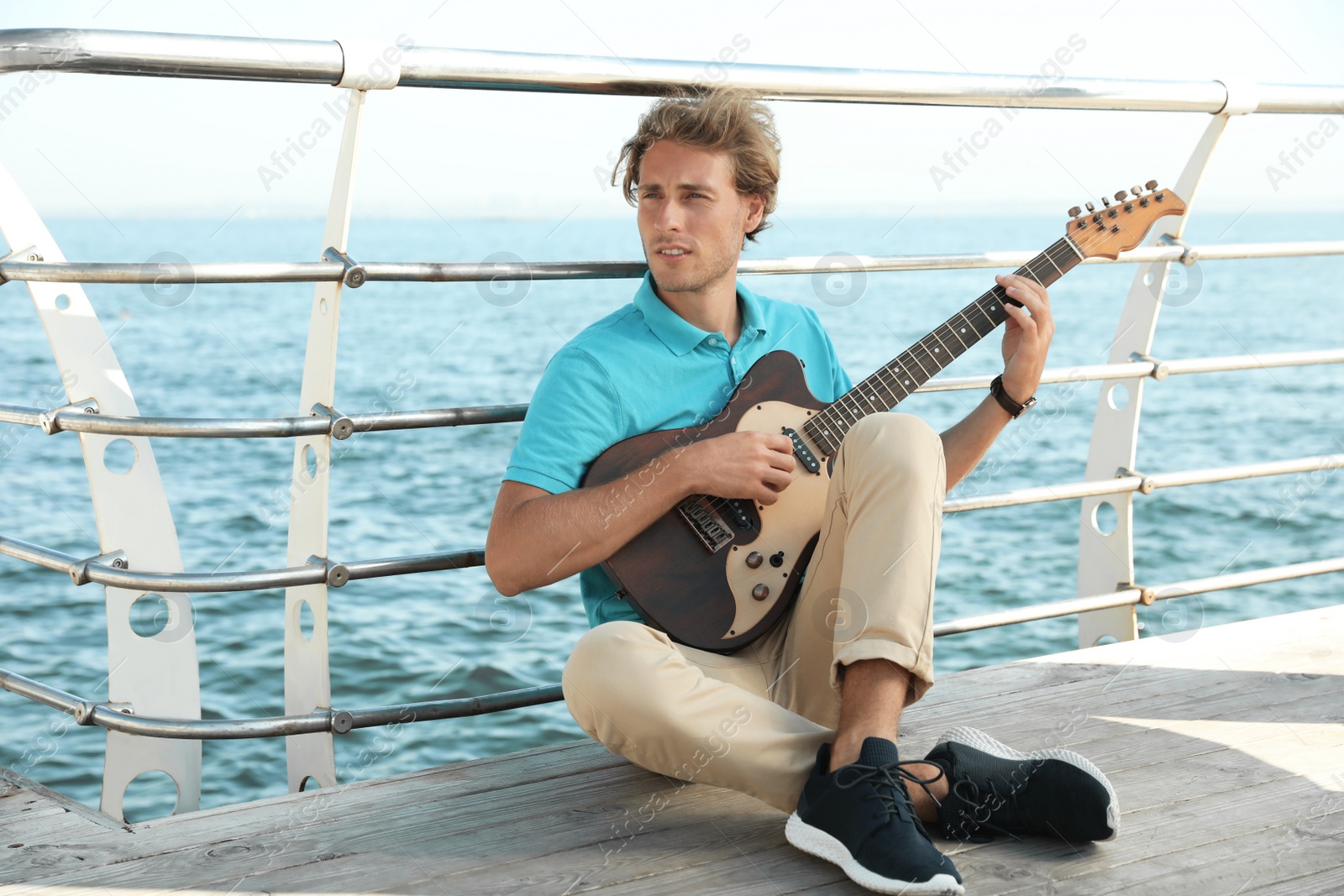 Photo of Portrait of handsome young man with guitar on sea pier