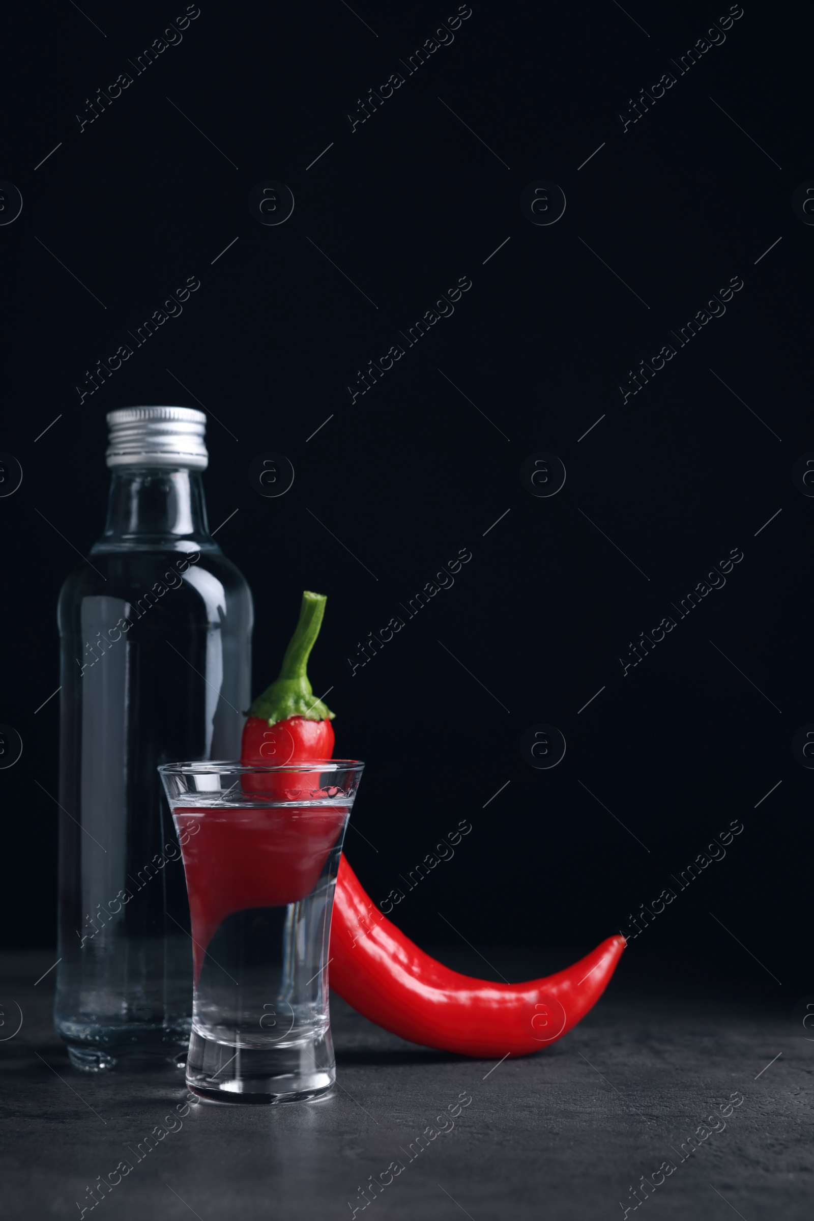 Photo of Red hot chili peppers and vodka on grey table against black background, space for text