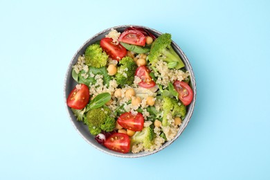 Photo of Healthy meal. Tasty salad with quinoa, chickpeas and vegetables on light blue table, top view