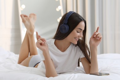 Photo of Young woman in white t-shirt and underwear listening to music on bed indoors