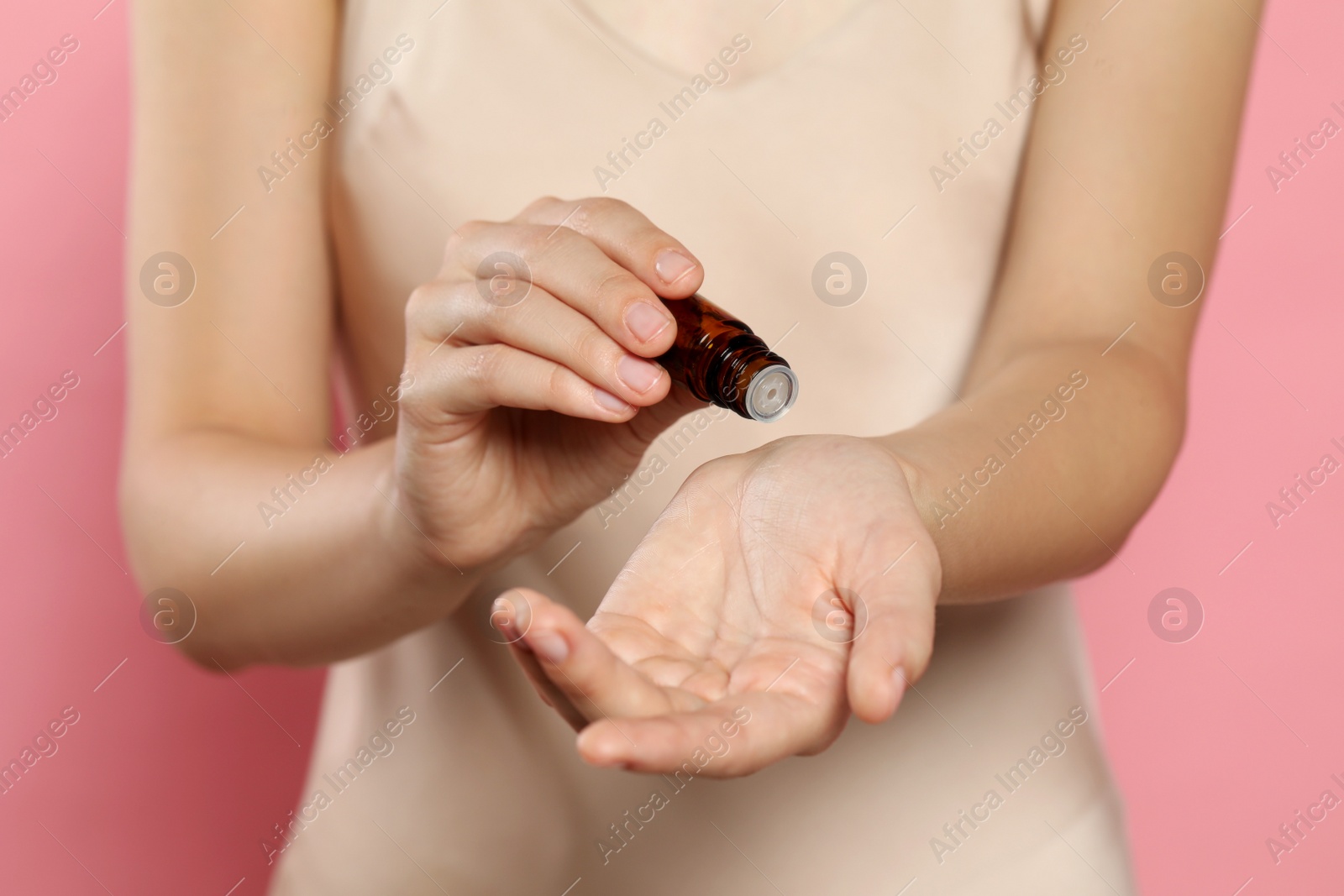 Photo of Young woman applying essential oil onto wrist on pink background, closeup