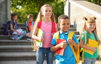 Photo of Cute little children with backpacks and notebooks outdoors. Elementary school