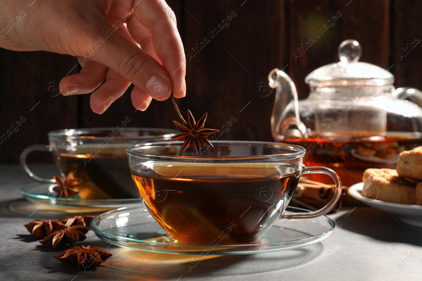 Photo of Woman putting anise star into cup of tea on light grey table, closeup