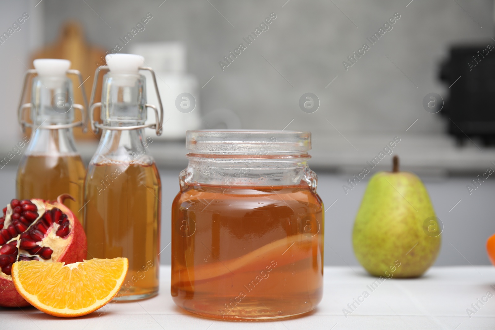 Photo of Homemade fermented kombucha and fresh fruits on white table in kitchen